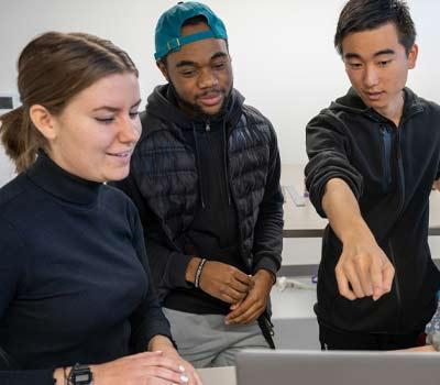 3 students gathered around a laptop